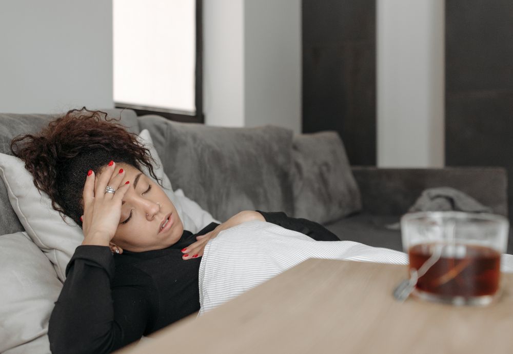 A person lying on the sofa looking ill with a cup of tea