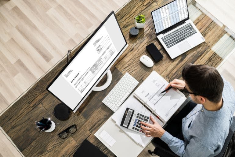 A man working on laptop with calculator nearby, doing payroll calculations